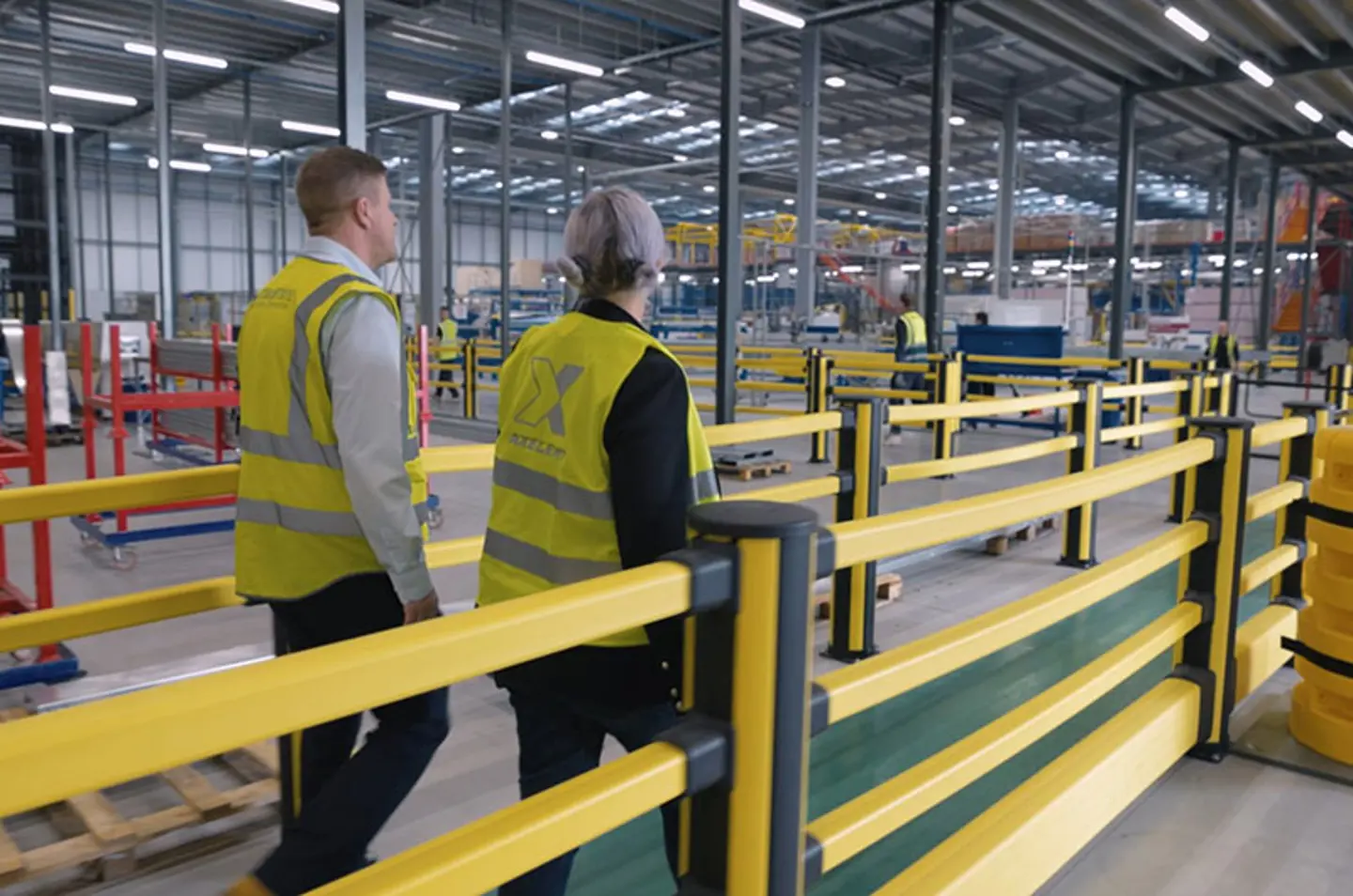 Barrières de sécurité protégeant les allées piétonnes dans un entrepôt moderne, avec des travailleurs portant des gilets de sécurité jaunes.
