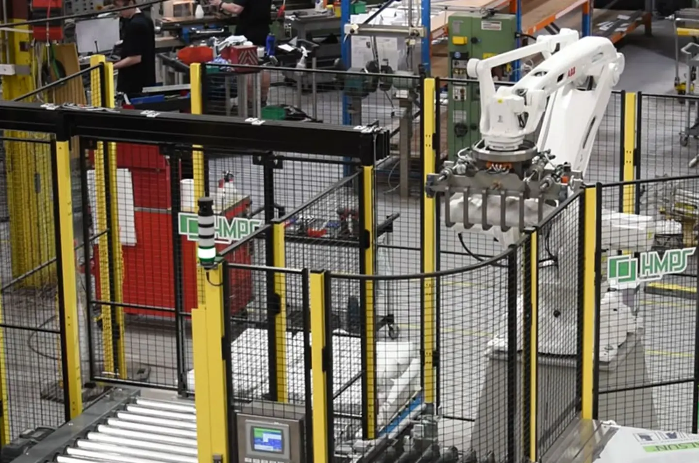 Bras robotisé industriel automatisé fonctionnant dans une usine avec systèmes de convoyeurs et clôtures de sécurité.