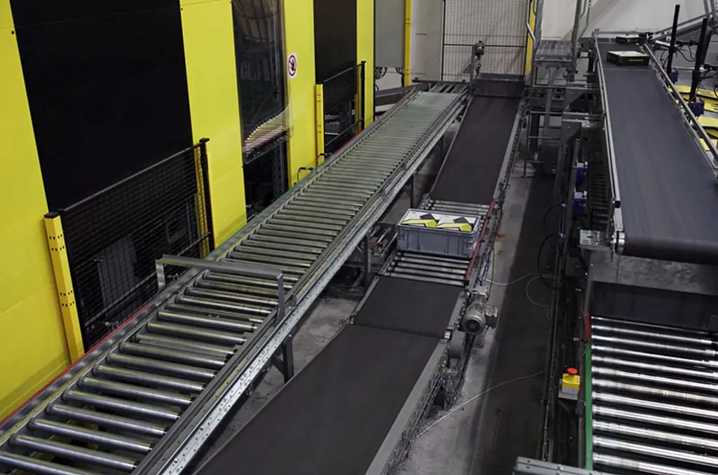 Système de tri automatisé en entrepôt avec convoyeurs et clôtures de sécurité, conçu pour la logistique à grande vitesse.